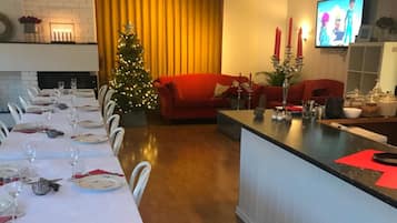 A dining area with a long table set for a meal, a Christmas tree, and a red sofa in the background.