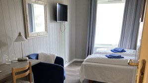 A hotel room with a bed, a desk with a chair, a TV, and a window with curtains. - Førde Pensjonat (Sunnfjord)
