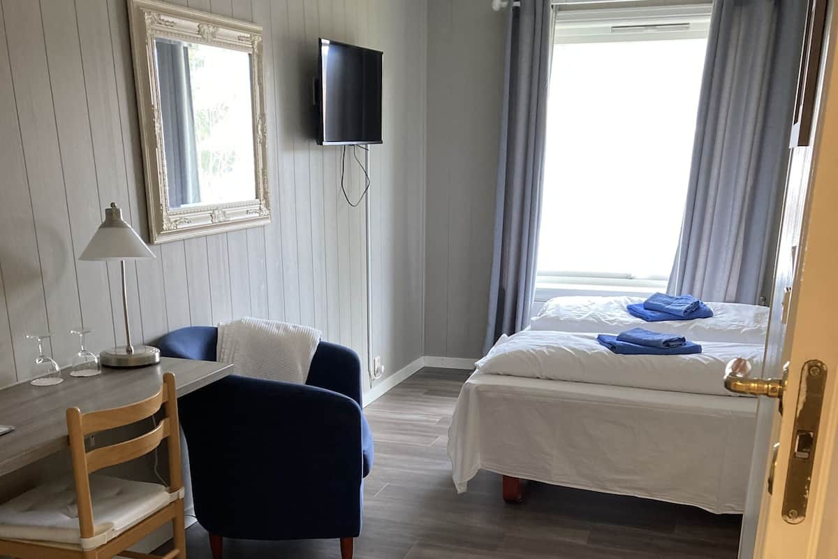 A hotel room with a bed, a desk with a chair, a TV, and a window with curtains.