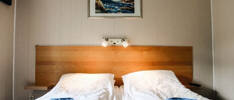 Una cama doble con ropa de cama blanca, un cabecero de madera y un cuadro de un paisaje marino en la parte superior.