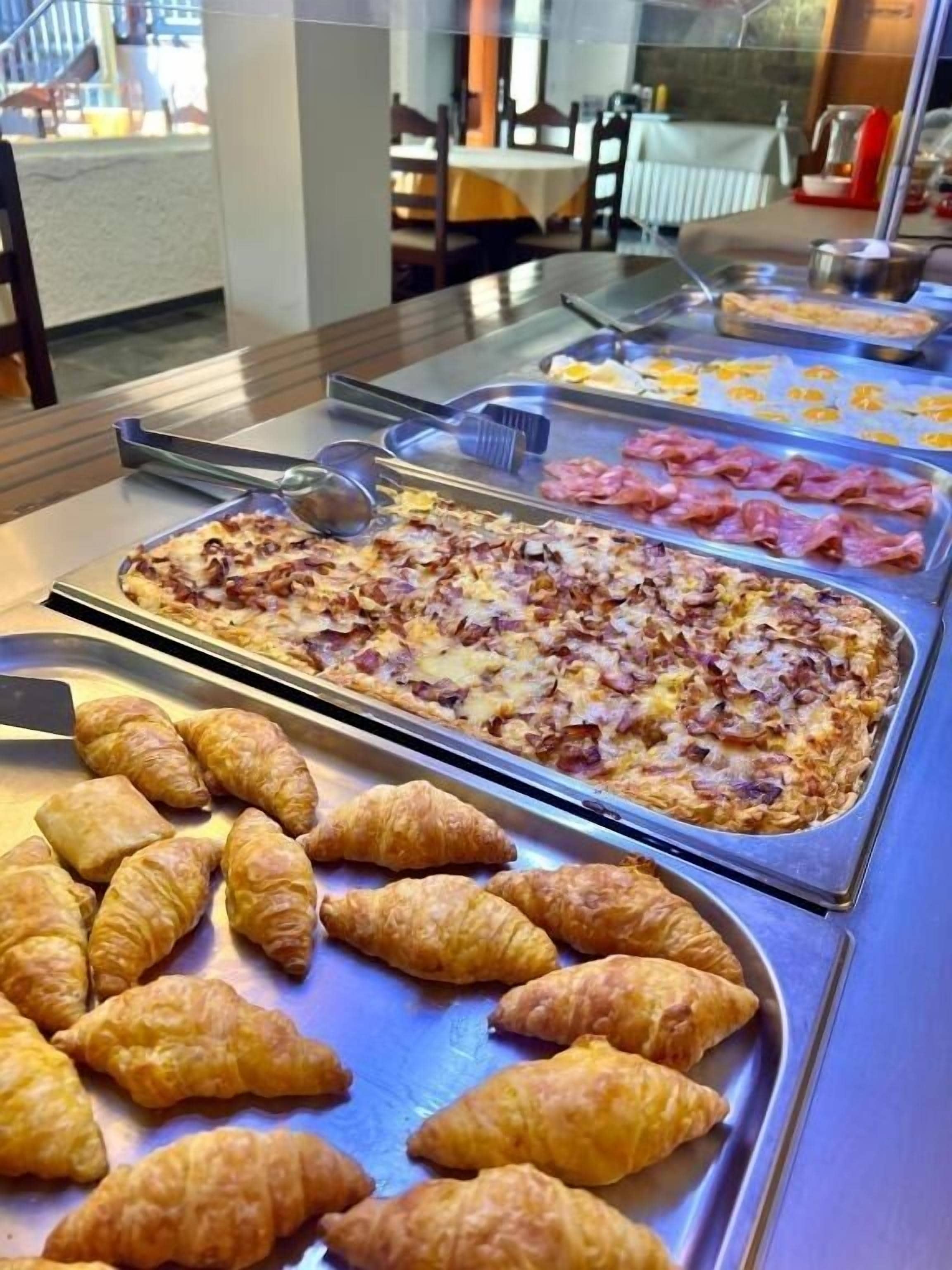 Een buffet met diverse gerechten, waaronder pizza, ham en croissants.