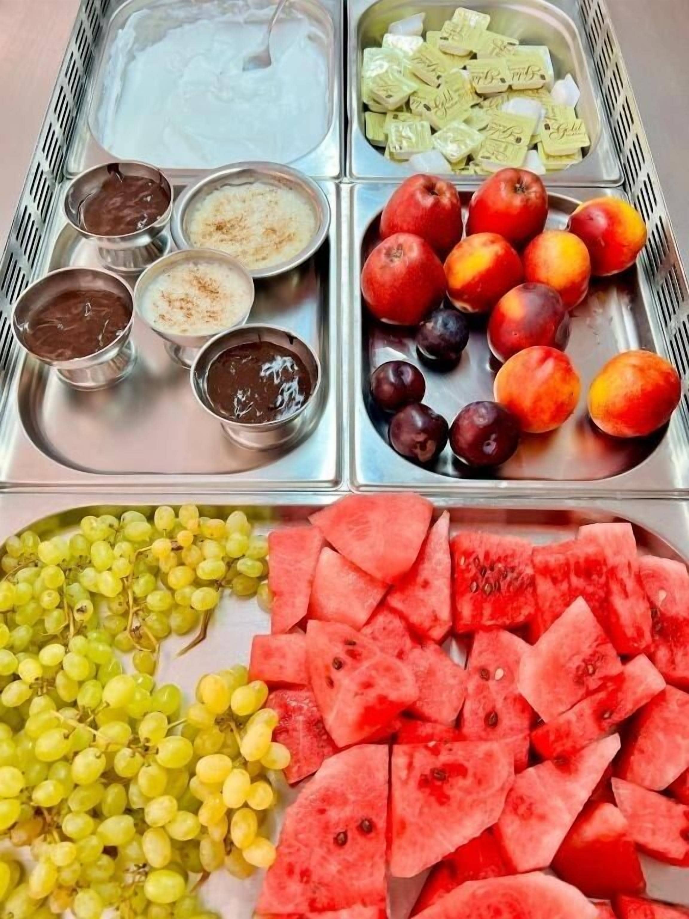 A tray with various fruits and dips, including grapes, watermelon, apples, and plums.