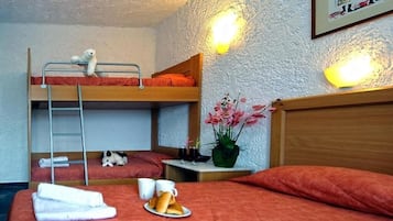 A dormitory room with bunk beds, a small table with a vase of flowers, and a breakfast tray on the lower bunk.
