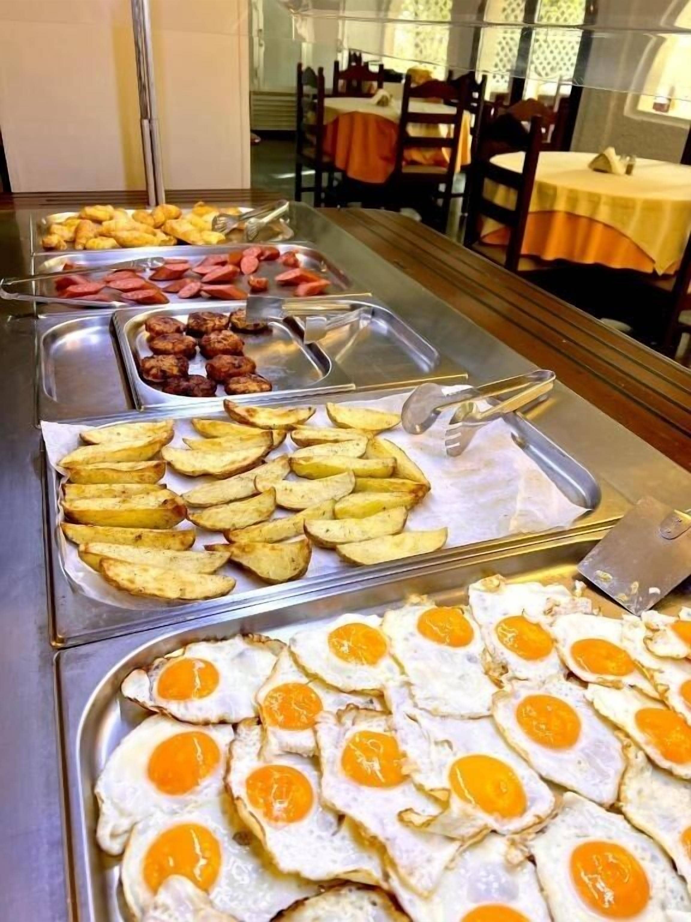 A buffet with various food options including sausages, potatoes, and fried eggs.