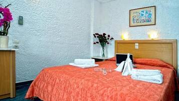 Ein Hotelzimmer mit einem Bett, einem Nachttisch mit Blumenvase, einem gerahmten Bild an der Wand und einem Beistelltisch mit Lampe.