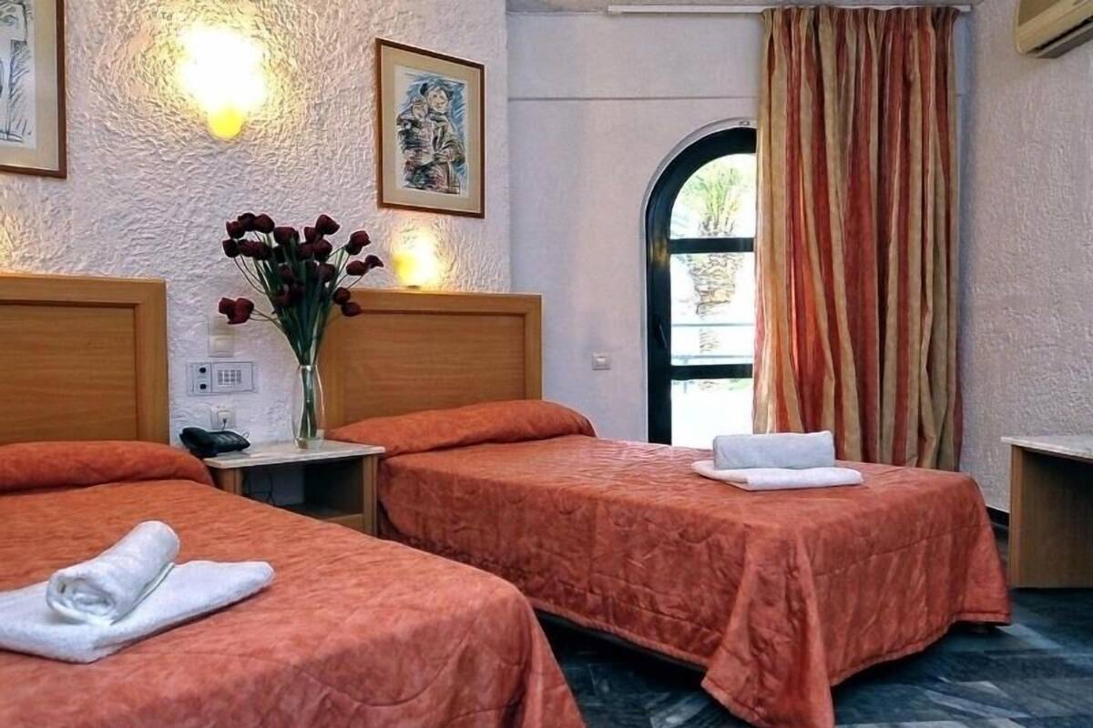 Habitació d'hotel amb dos llits, un ram de flors, un quadre i una vista per la finestra.