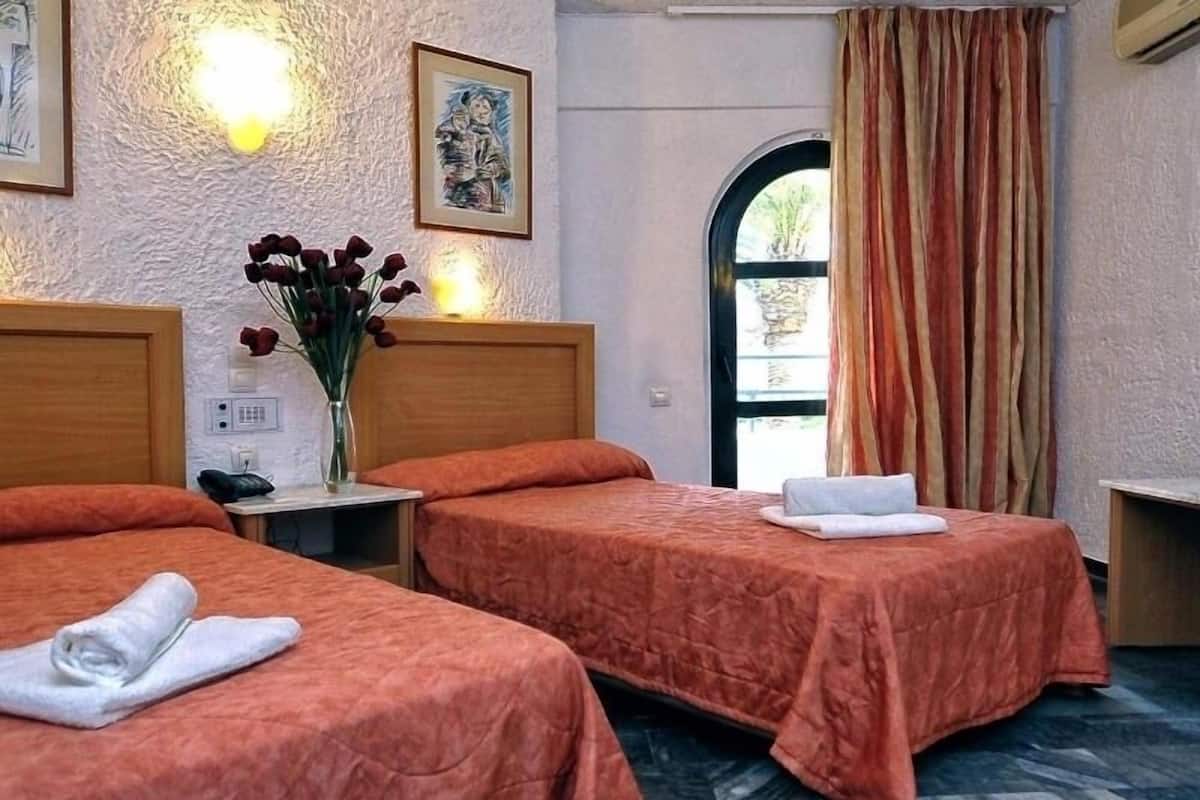 A hotel room with two beds, a vase with flowers, a painting, and a view through a window.