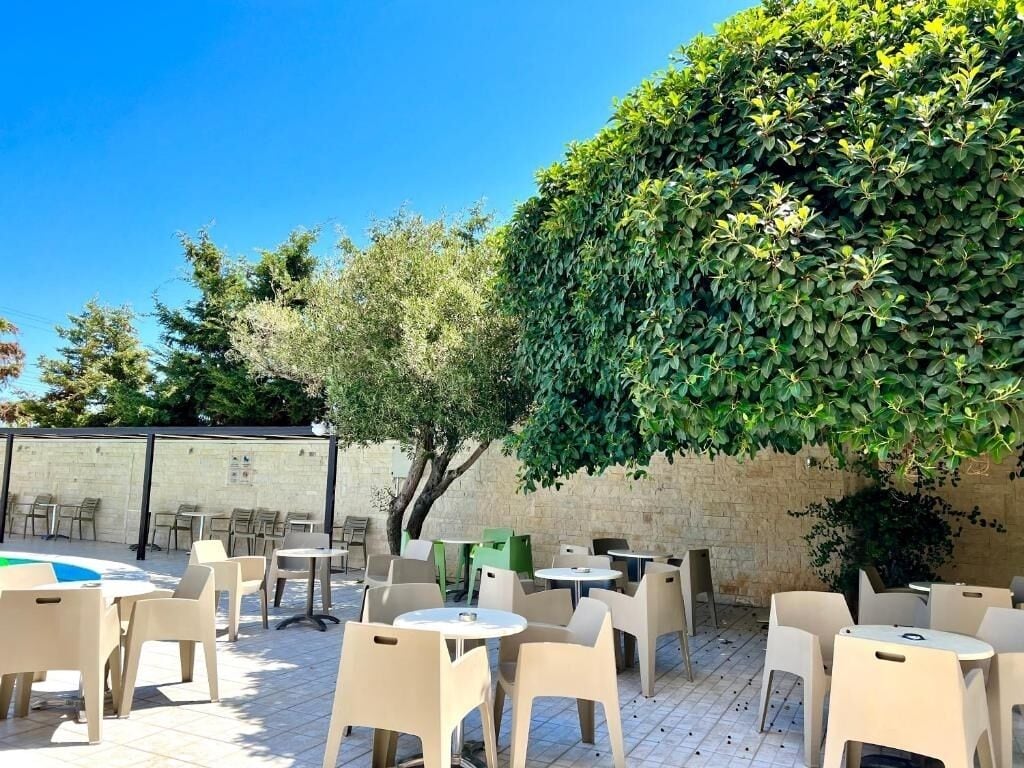 An outdoor patio with round tables and chairs, surrounded by a brick wall and greenery.