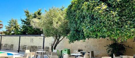Une terrasse extérieure avec des tables et des chaises rondes, entourée d’un mur de briques et de verdure.