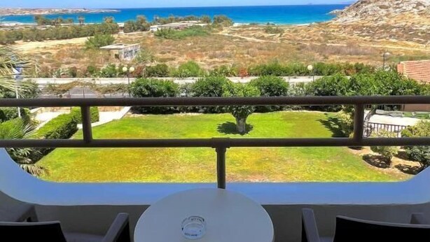 Een balkon met een tafel en stoelen, met uitzicht op een kustlandschap en een helder zicht op de zee en heuvels in de verte.