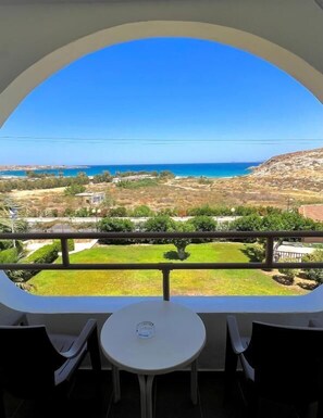 Un balcón con mesa y sillas, con vista a un paisaje costero que ofrece una vista despejada del mar y colinas distantes.