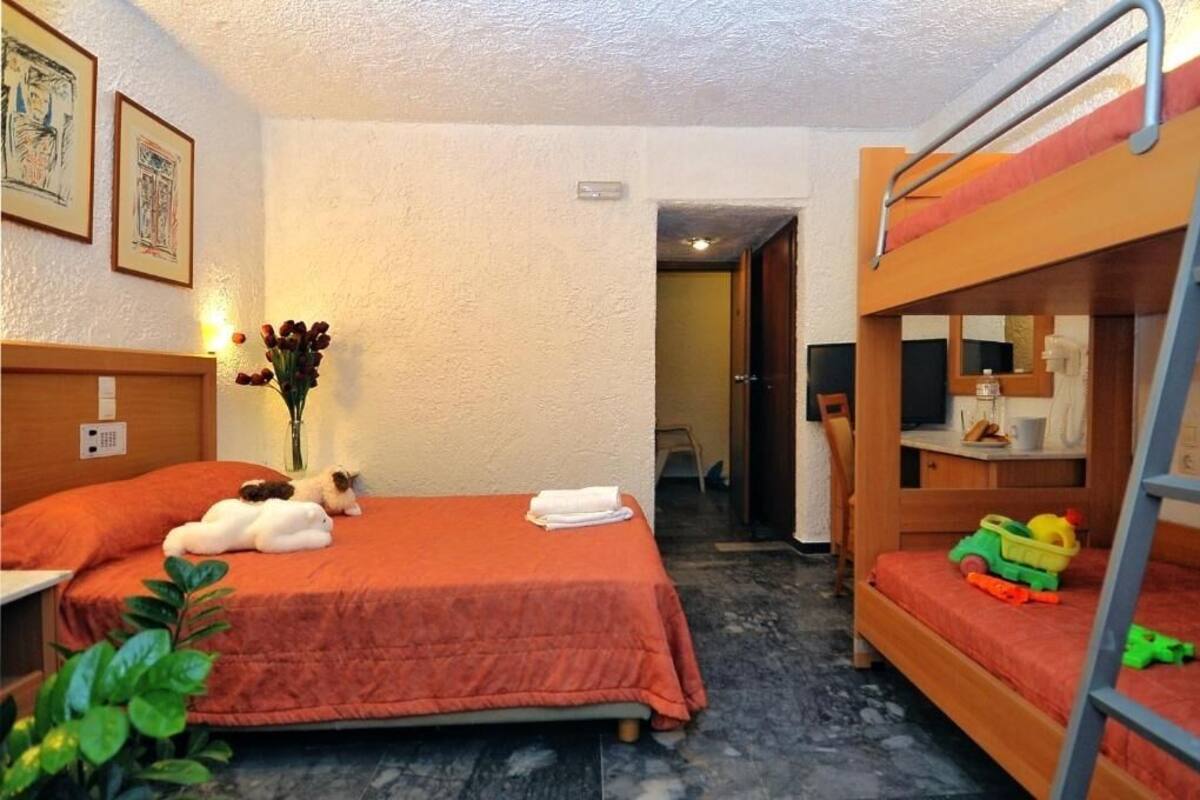Habitació d'hotel amb lliteres, un llit amb llençol vermell, una petita taula d'escriptori amb mirall i un ram de flors.