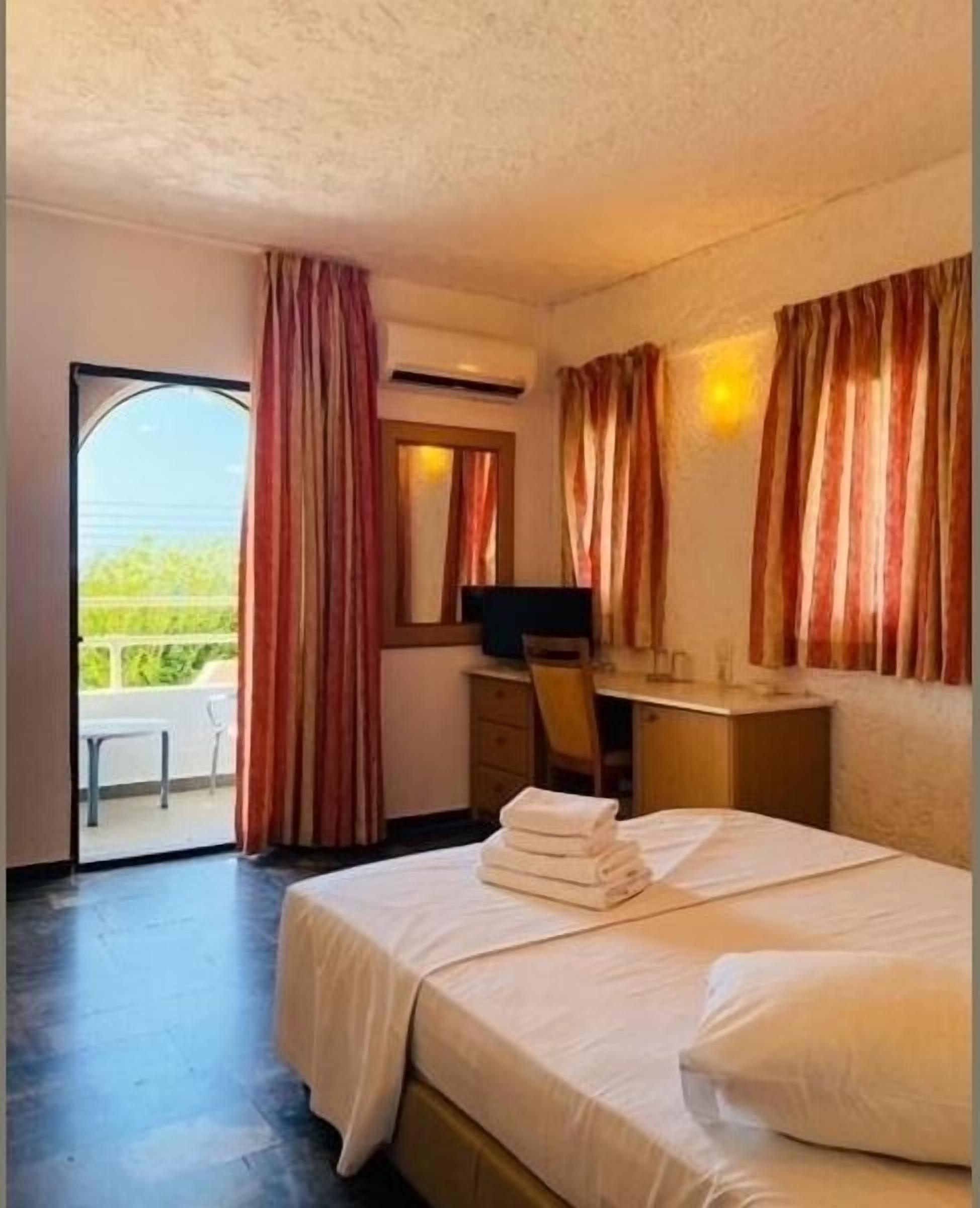 Habitación de hotel con cama, escritorio, silla, equipo de aire acondicionado y vistas al exterior.