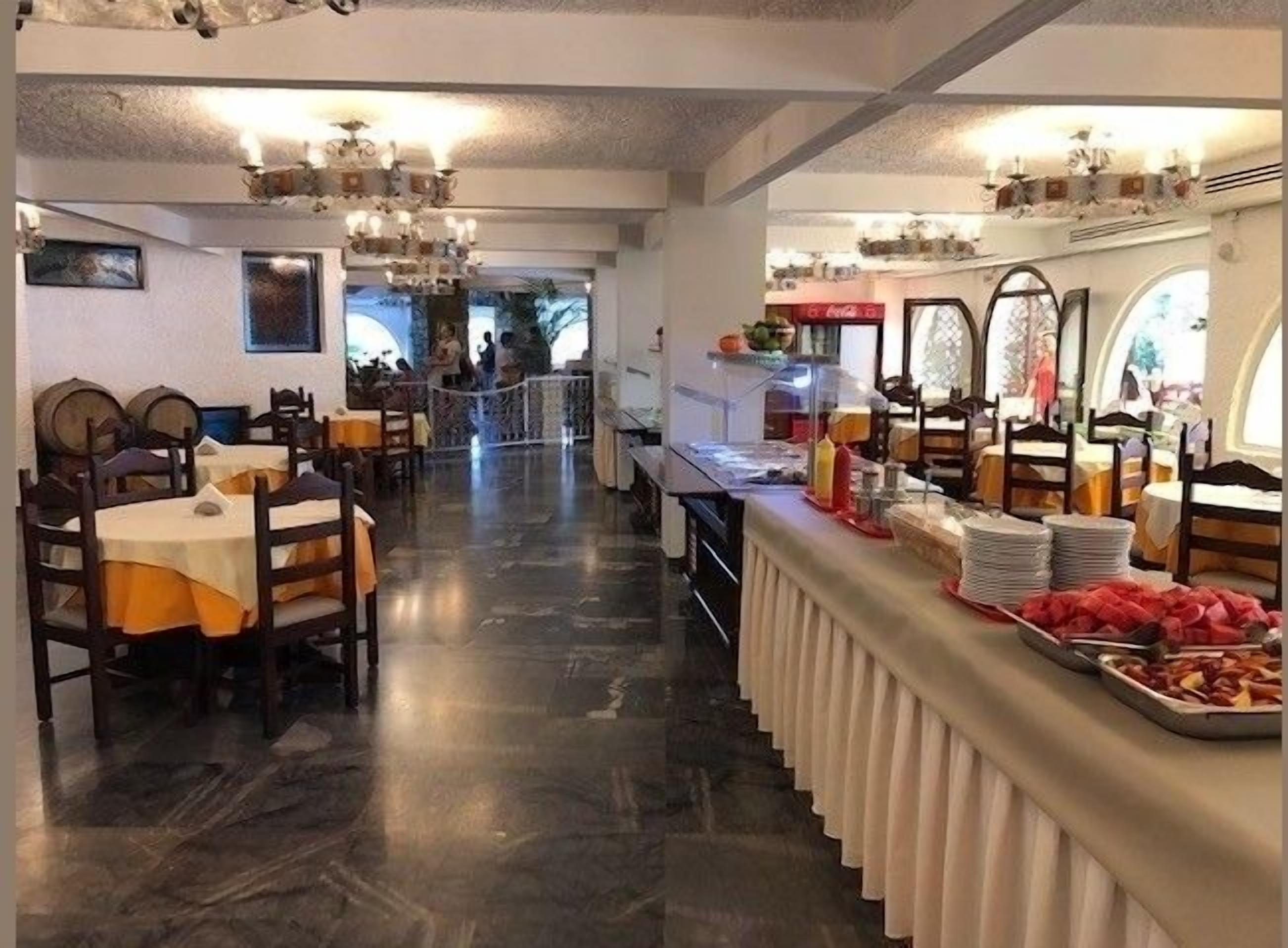 A restaurant with a long counter, multiple tables, and a chandelier.