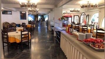 A restaurant with a long counter, multiple tables, and a chandelier.
