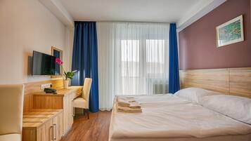 Una camera d'albergo con un letto, una scrivania con una sedia, una TV e una finestra con tende.