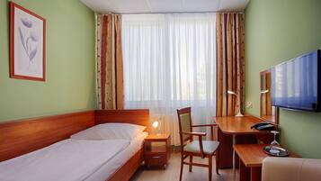 A hotel room with a bed, a desk with a chair, a television, and a window with curtains.