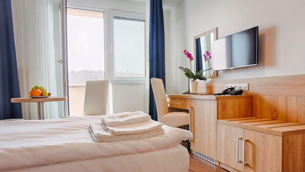 A hotel room with a bed, a desk, a chair, a TV, and a window with curtains. - Ensana Spa Smrdaky (Smrdáky)