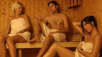 Three people sitting in a sauna with wooden walls and benches.