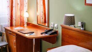 A hotel room with a wooden desk, a telephone, a lamp, a mirror, and a bed.