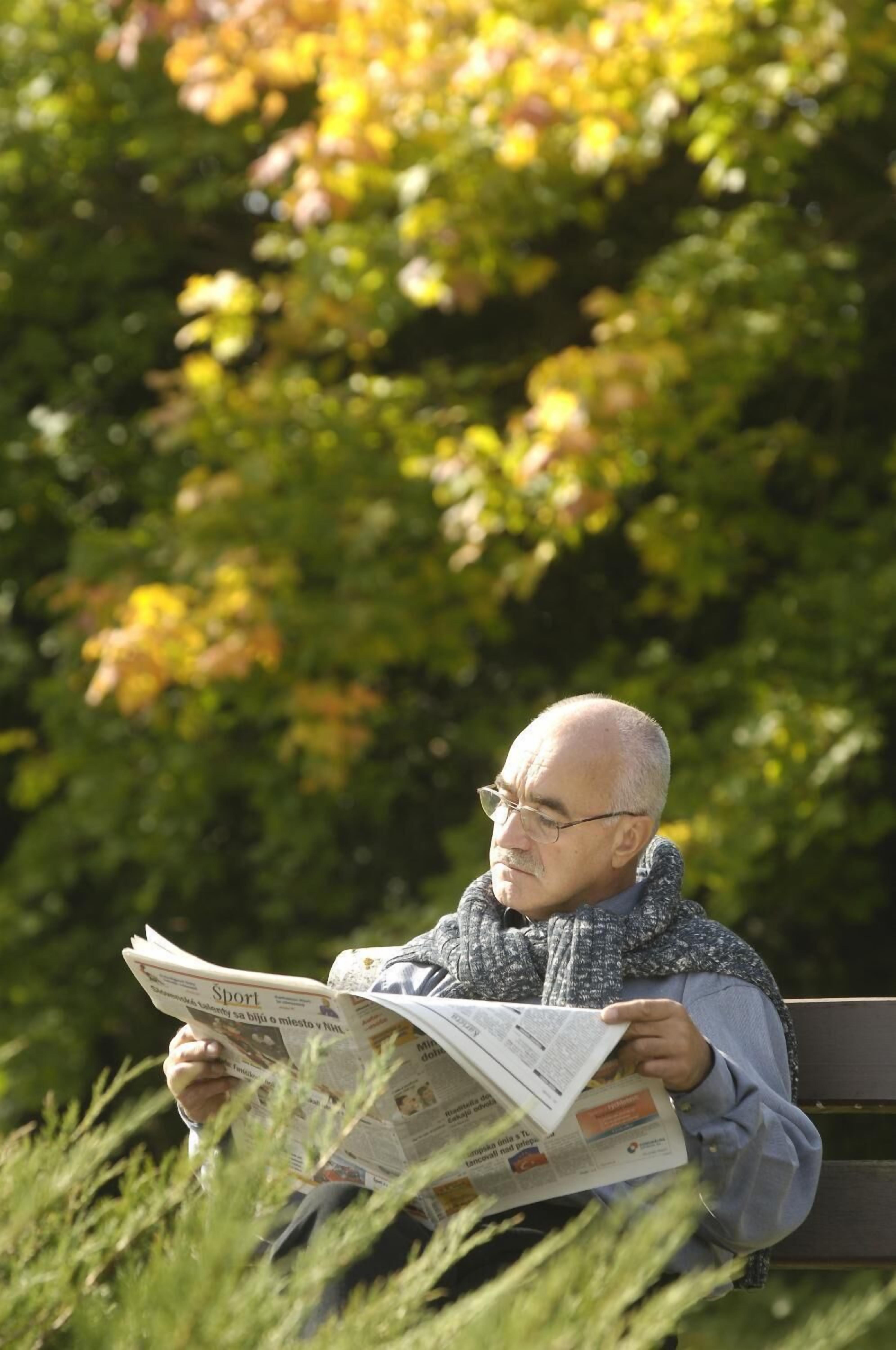 Eine Person sitzt auf einer Bank und liest eine Zeitung.