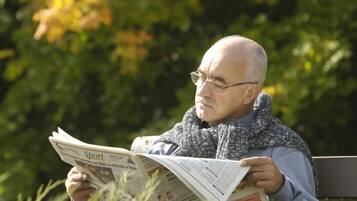 Eine Person sitzt auf einer Bank und liest eine Zeitung.