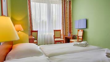 Une chambre d’hôtel avec deux lits, un bureau avec une chaise, un téléviseur fixé au mur et une fenêtre avec des rideaux.