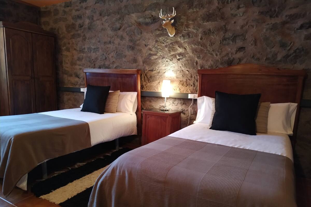 A room with two beds, wooden headboards, a stone wall, and a mounted deer head.