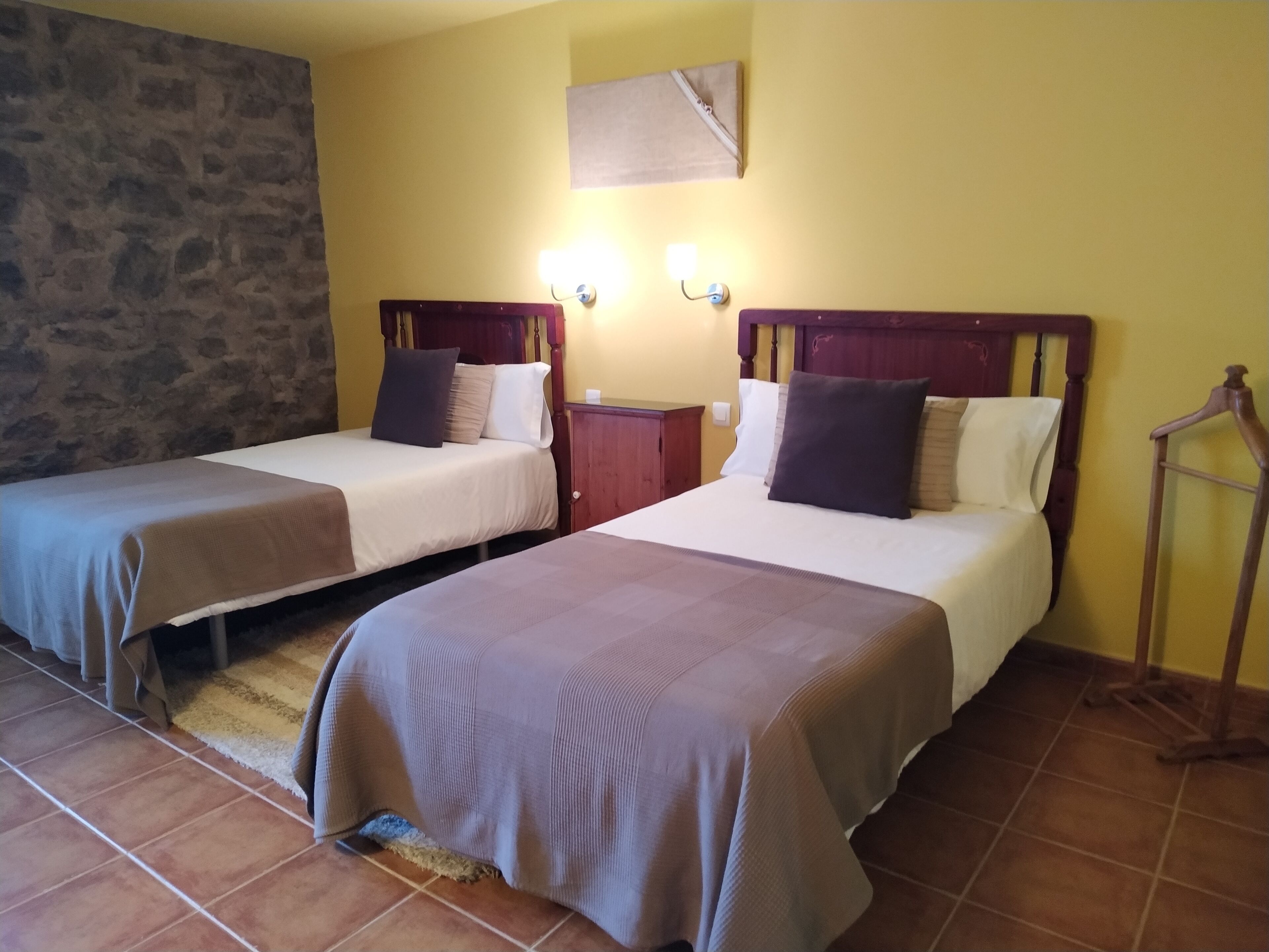 Una habitación con dos camas, una pared de piedra, un armario de madera y una mesita de noche con lámpara.