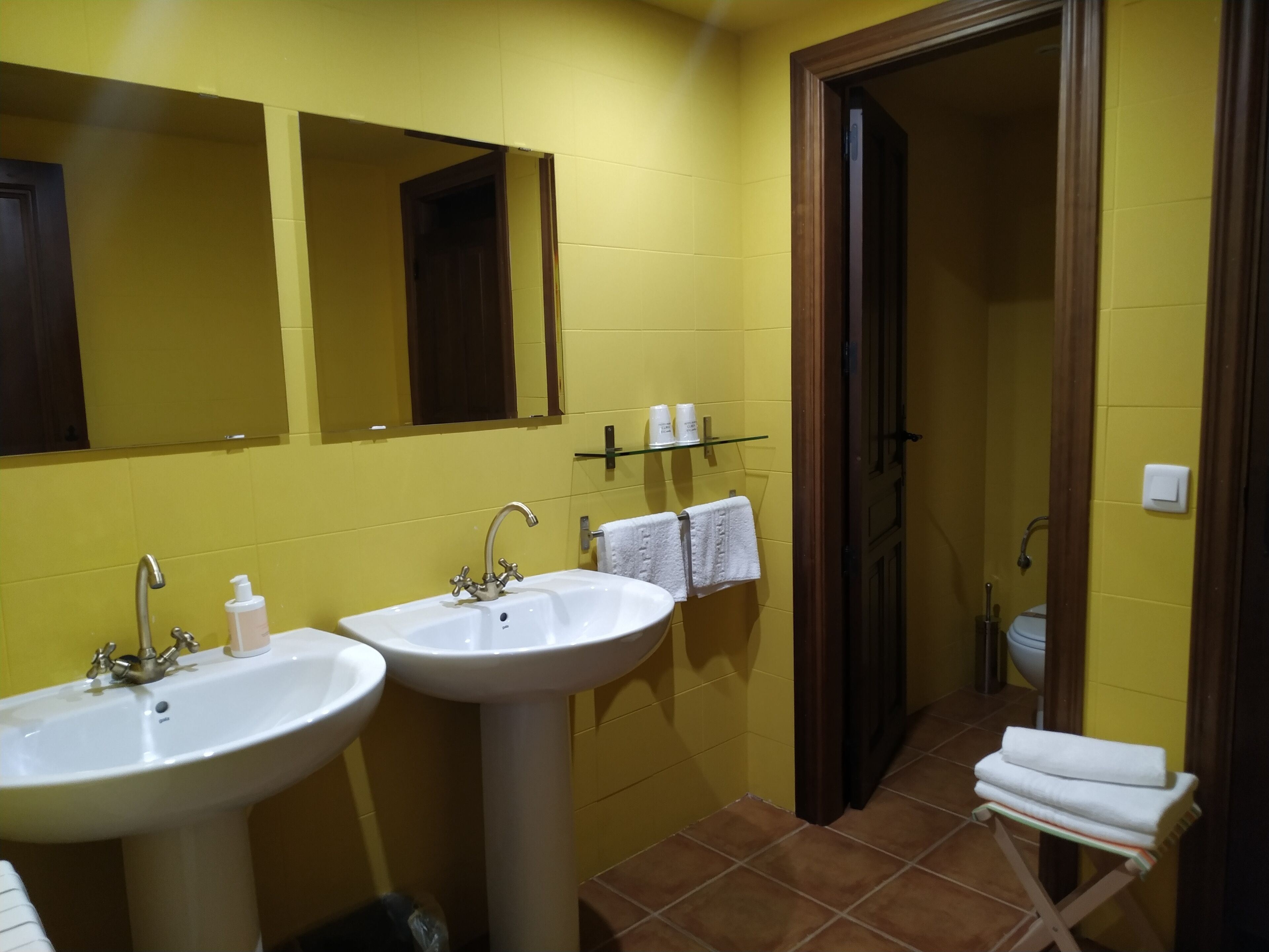 Un baño con dos lavamanos, un espejo y un estante con artículos de aseo.