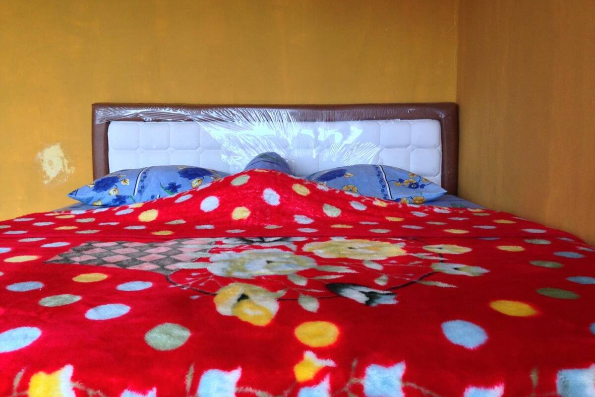A bed with a red polka dot blanket and floral pillows, a white headboard, and a yellow wall.