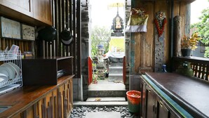 Un couloir étroit doté d’un plancher en bois, une petite marche menant à un sanctuaire, et un coin cuisine avec des ustensiles suspendus et un égouttoir à vaisselle.