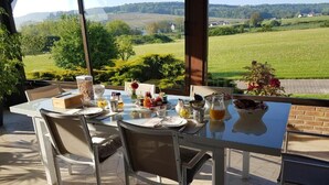 Un espace de restauration en plein air avec une table dressée pour le petit-déjeuner, offrant une vue panoramique sur la campagne environnante.