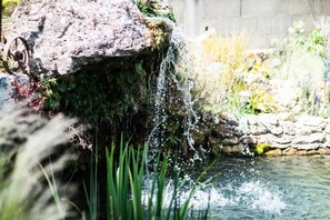 A waterfall feature with a rustic stone structure, surrounded by lush greenery and a stone wall.