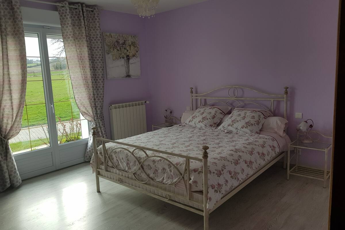 Une chambre à coucher avec un lit, une table de chevet, un radiateur et une fenêtre avec des rideaux.