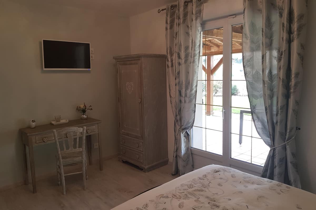 Une chambre à coucher comprenant un lit, une armoire en bois, un bureau avec une chaise et un téléviseur fixé au mur.