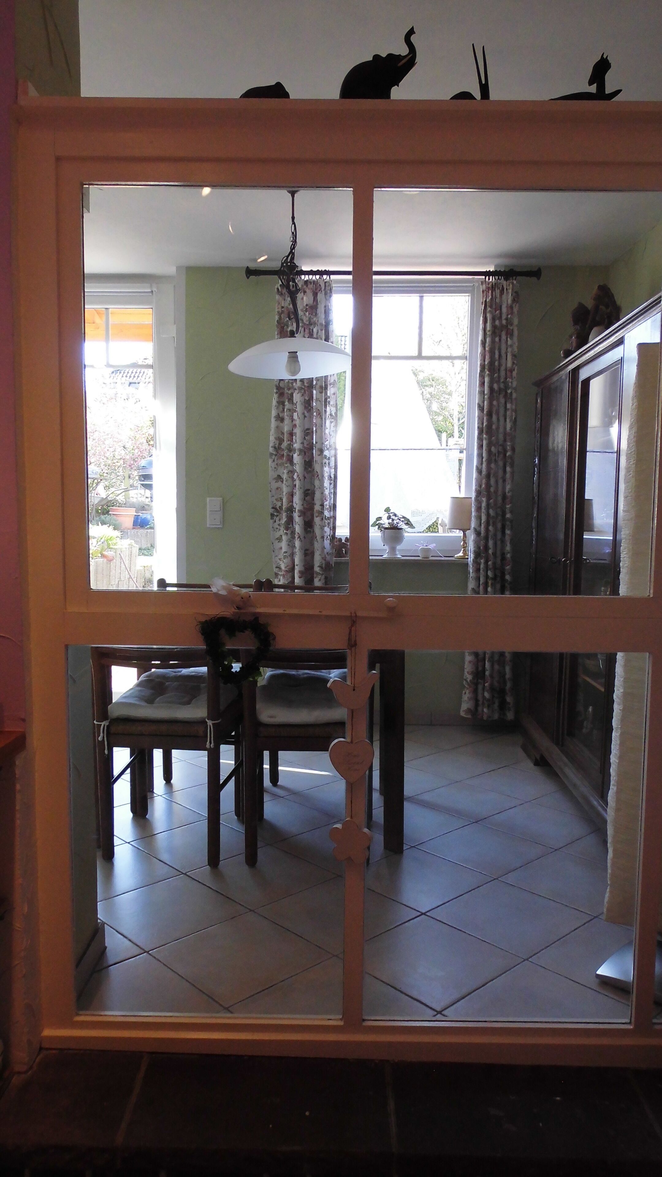 Un comedor con una mesa y sillas, una lámpara colgante, y vistas al exterior, a un espacio con plantas, a través de una puerta de vidrio.