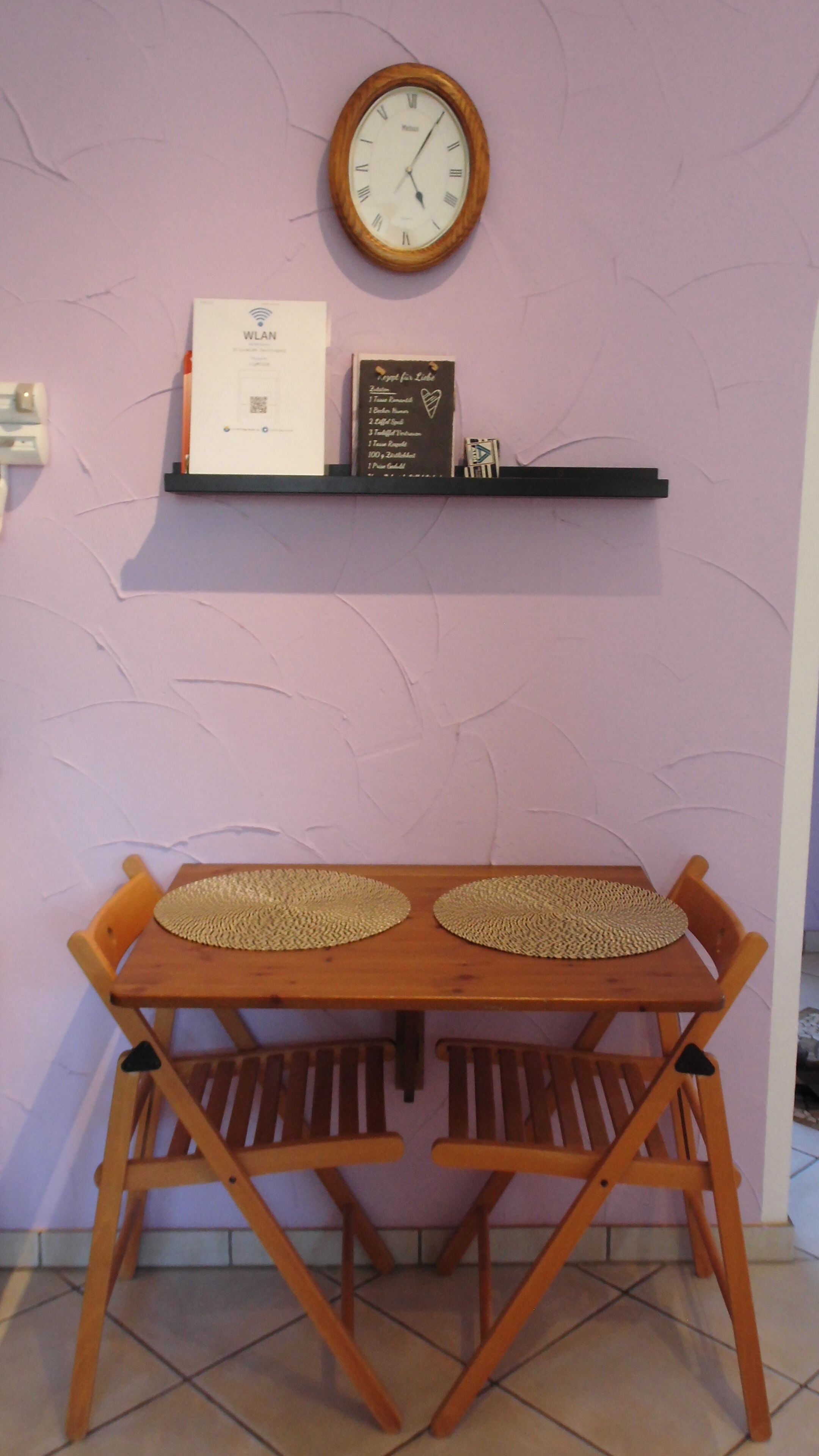 Een tafel met twee stoelen, een wandklok, een plank met een bord en een QR-code.