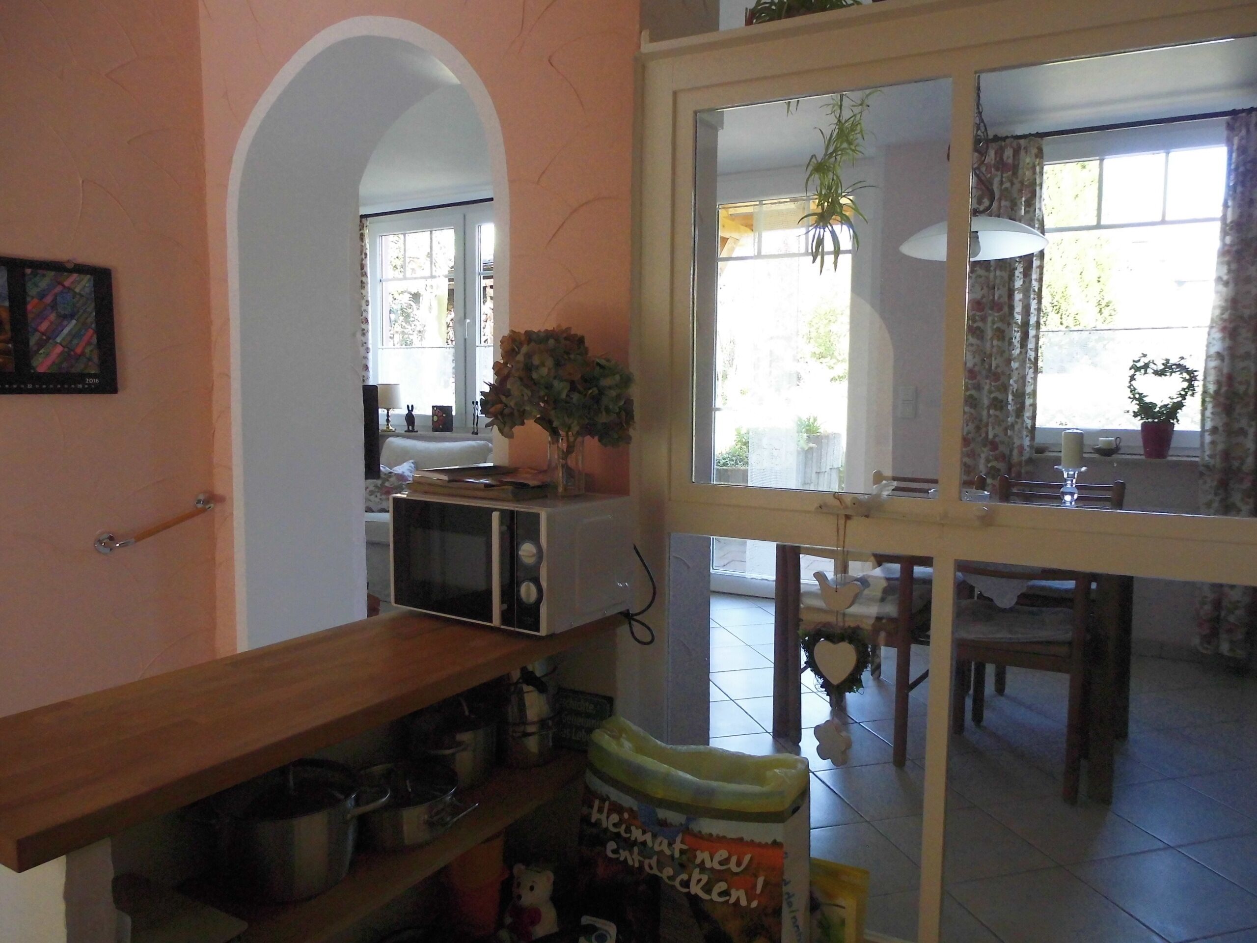 Una cocina con microondas, una repisa de madera con utensilios de cocina y una ventana con cortinas.