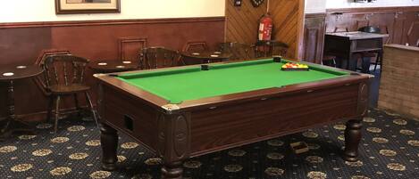 A billiards room with a pool table, chairs, and framed pictures on the walls.