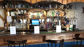 A bar area with wooden bar counters, multiple liquor bottles, and bar stools. - Dinorben Arms Hotel (Amlwch)