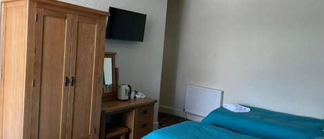Un dormitorio con dos camas, un armario de madera, un escritorio con hervidor y un televisor en la pared.