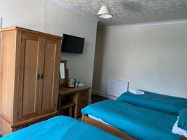 Un dormitorio con dos camas, un armario de madera, un escritorio con hervidor y un televisor en la pared.