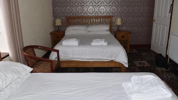 Habitación de hotel con cama doble, dos mesitas de noche con lámparas, una silla de madera y papel tapiz estampado.