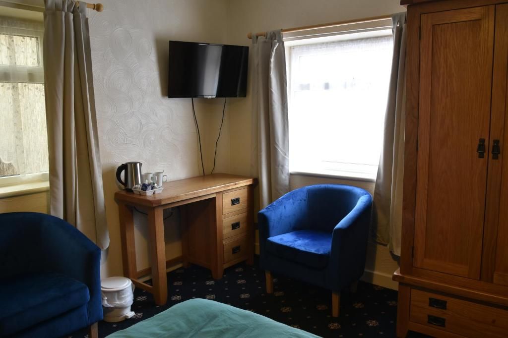 A hotel room with a desk, a blue armchair, a television, and a wardrobe.