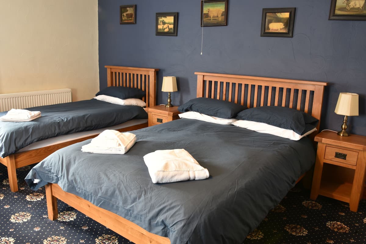 A hotel room with two single beds, each with a wooden headboard, a bedside table with a lamp, and a neatly folded towel on each bed.