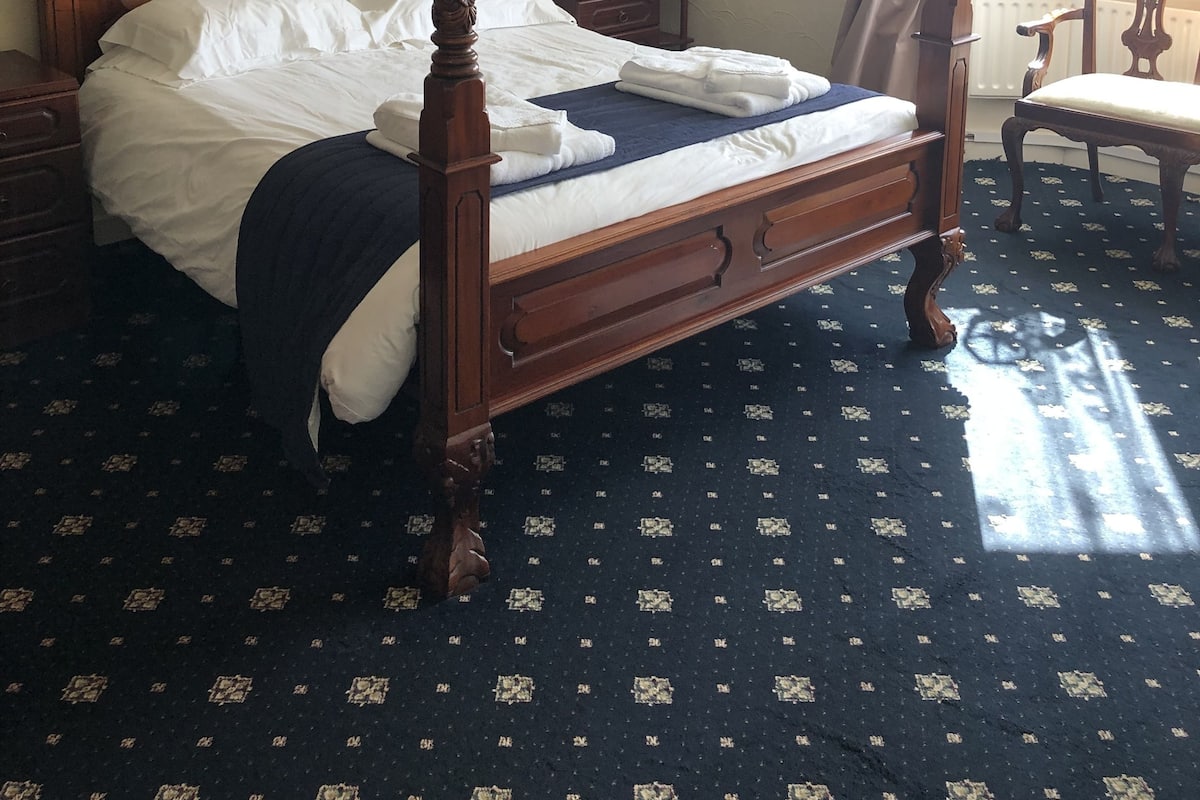 A four-poster bed with a lace canopy, a chandelier, a small table with a lamp, and a chair.