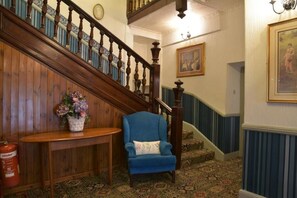 A wooden staircase with a blue chair and a small table with a vase of flowers. - Dinorben Arms Hotel (Amlwch)