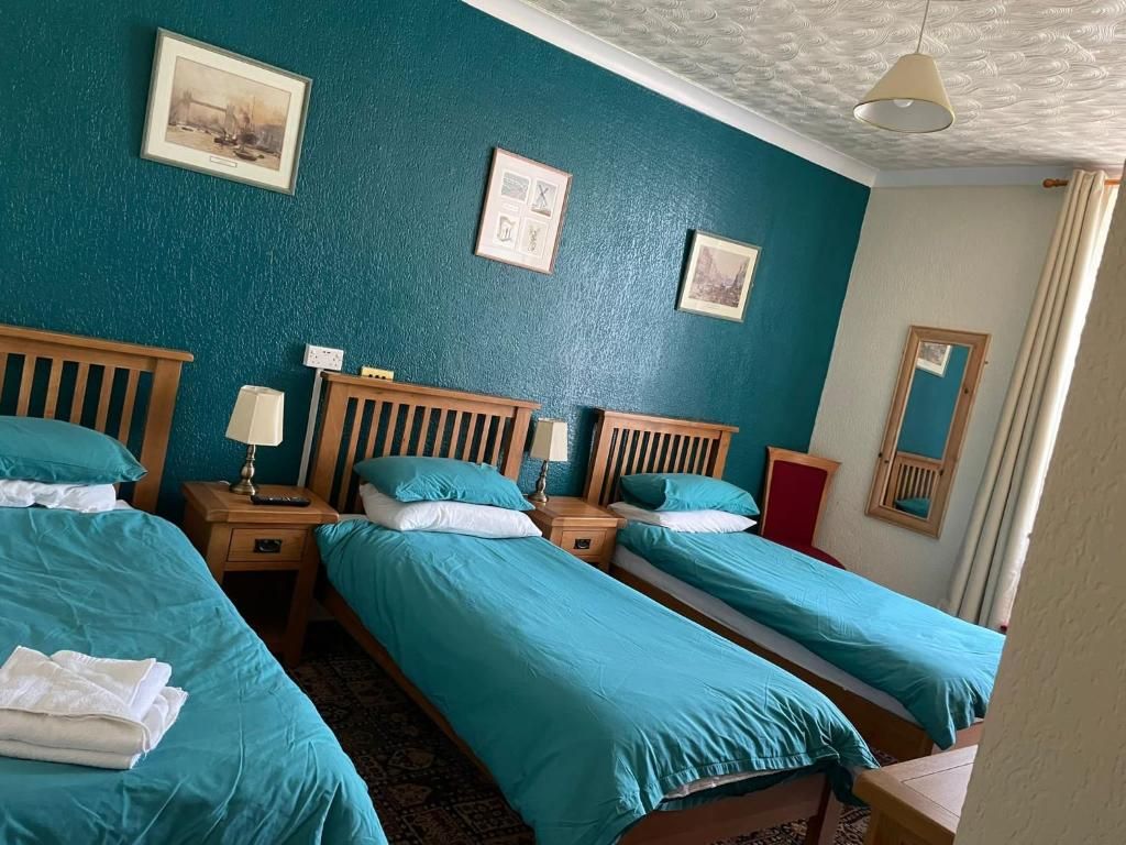 Een hotelkamer met drie eenpersoonsbedden, een houten hoofdbord, een nachtkastje met een lamp en een ingelijst schilderij aan de muur.