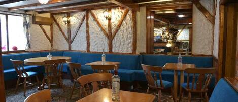 Een restaurantinterieur met houten balken, blauwe gestoffeerde zitplaatsen en ronde tafels.